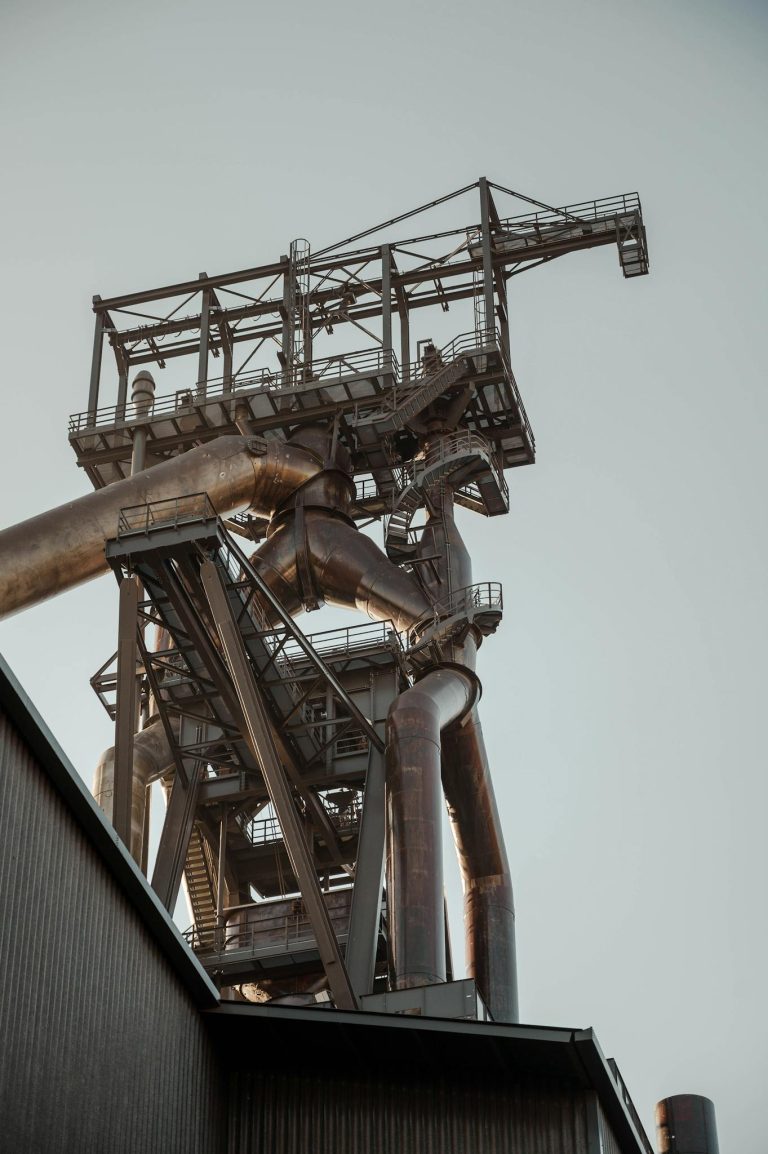 Low angle view of an industrial structure with metal pipes and framework against a clear sky.